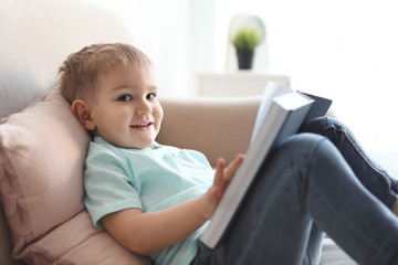 Cute child reading book on sofa indoors