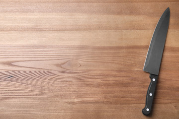 Sharp chef's knife on wooden table, top view with space for text