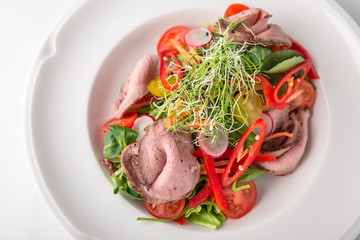 Salad of ham, prosciutto, pork or beef with vegetables, greens, berries and sauce. Nutritious, healthy dish. Banquet festive dishes. Gourmet restaurant menu. White background.