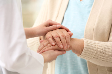 Nurse comforting elderly woman against blurred background, closeup. Assisting senior generation