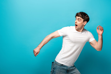 scared young man running away and looking back on blue background