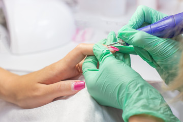 Manicurist, nail artist handles nails with manicure milling cutter. Beauty service, nail salon, health care and cosmetics