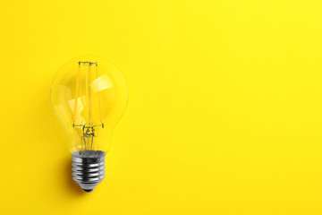 Vintage filament lamp bulb on yellow background, top view. Space for text