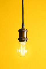 Hanging modern lamp bulb against yellow background