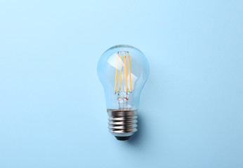 New modern lamp bulb on light blue background, top view