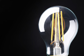 New modern lamp bulb on black background, closeup. Space for text