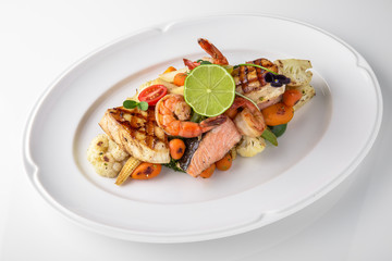 Luxurious seafood salad of shrimp, grilled salmon fillet, sea bream, grilled vegetables and lime. Banquet festive dishes. Fine dining restaurant menu. White background.