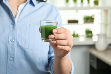 Woman holding shot glass of wheat grass juice indoors, closeup