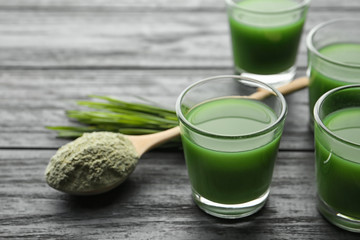 Glasses of wheat grass juice and spoon with powder on wooden table. Space for text