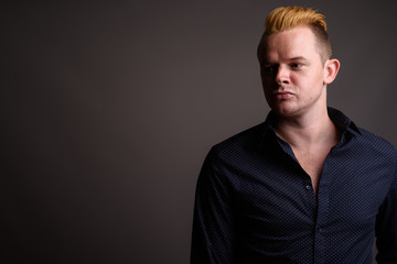 Businessman with Mohawk hairstyle and blond hair against gray ba