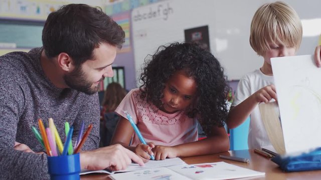 Elementary School Teacher Giving Female Pupil One To One Support In Classroom 