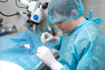Naklejka na ściany i meble A professional ophthalmologist performs eye surgery with a microscope. The doctor inserted the dilator into the eye, washes and removes pus with a syringe. Endoscopic eye surgery. medical equipment