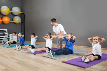 Trainer helping children to do physical exercise in school gym. Healthy lifestyle