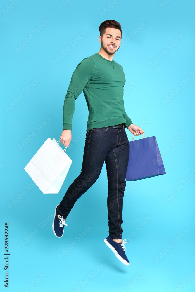 Canvas Prints full length portrait of young man jumping with paper bags on blue background