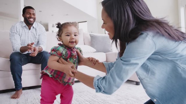 Parents At Home Encouraging Baby Daughter To Take First Steps