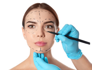 Doctor drawing marks on woman's face for cosmetic surgery operation against white background