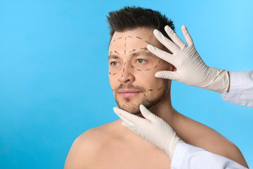 Doctor examining man's face before plastic surgery operation on blue background