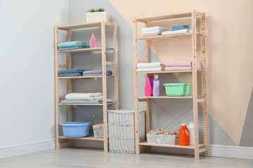 Wooden shelving units with clean towels and detergents in stylish room interior
