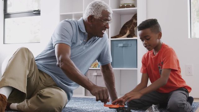 Grandfather With Grandson Sitting On Rug At Home Building Model Helicopter Together