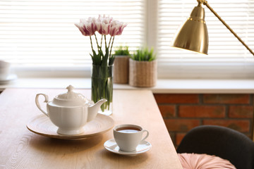 Tea set on table near window with blinds indoors