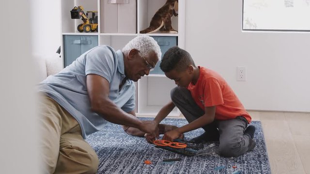 Grandfather With Grandson Sitting On Rug At Home Building Model Helicopter Together