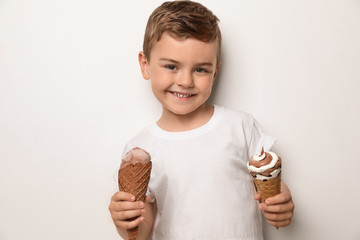 Adorable little boy with delicious ice creams against light background