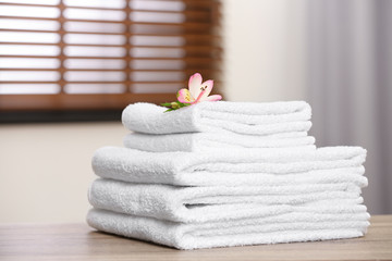 Pile of fresh towels and flower on wooden table in room