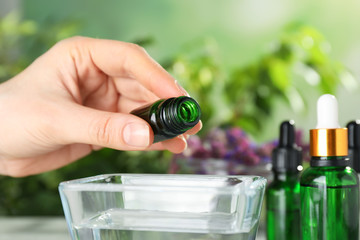 Woman dripping essential oil into bowl on table, closeup