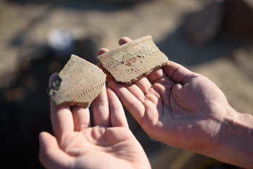 An archaeologist at an archaeological site shows fragments of ancient pottery in the hands of - obrazy, fototapety, plakaty