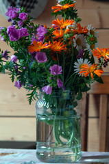 A bouquet of flowers stands in a transparent jar of water on a wooden table