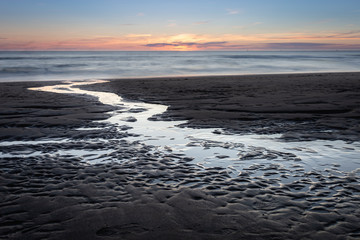 Beach after sunset during twilight. Water running from the beach to the sea with beautiful patterns in the sand.