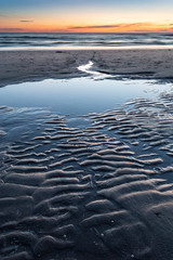 Beach after sunset during twilight. Water running from the beach to the sea with beautiful patterns in the sand.