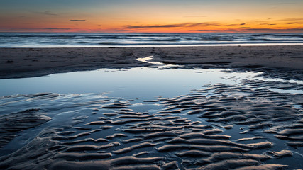 Beach after sunset during twilight. Water running from the beach to the sea with beautiful patterns in the sand.