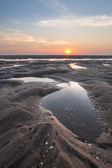 Sunset at the beach. sun just above the horizon on a sky with clouds. calm colors