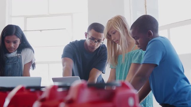 Students With Male Teacher In After School Computer Coding Class Learning To Program Robot Vehicle