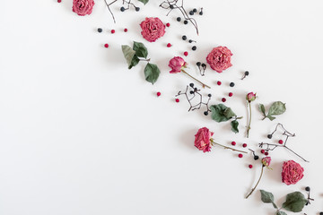 Autumn creative composition. Dried rose flowers, berries, leaves on white background. Autumn concept. Fall flower background. Flat lay, top view, copy space
