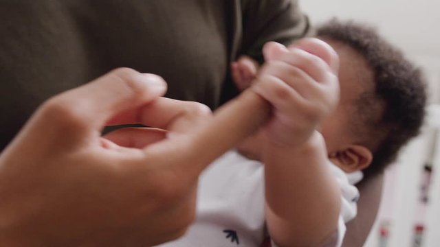 Baby Son Gripping Fathers Finger As He Cuddles Him In Nursery At Home