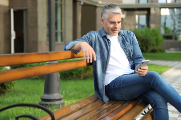 Fototapeta premium Portrait of handsome mature man using mobile phone in city. Space for text