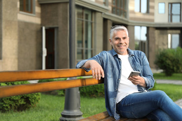Fototapeta premium Portrait of handsome mature man using mobile phone in city. Space for text