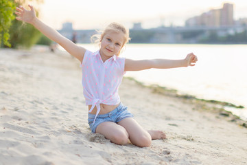 eight-year-old girl sitting on the sand and waving his hands . Family vacation on the beach in summer happy faces and smiles