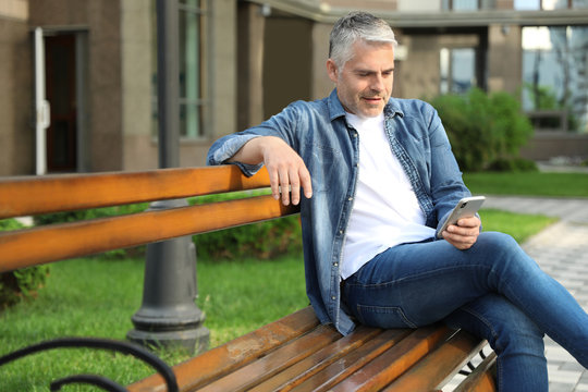 Portrait of handsome mature man using mobile phone in city. Space for text