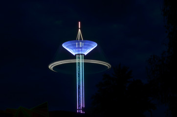 Attraction carousel on a long stock, multi-colored with light bulbs in night time, long exposure shooting in dark