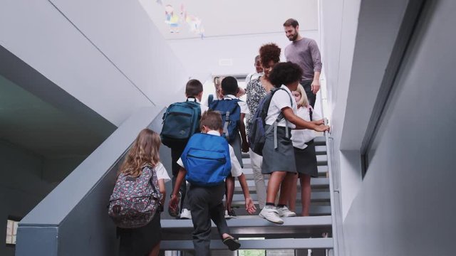 Teacher And Pupils Walking Down Stairs In Busy Elementary School Corridor