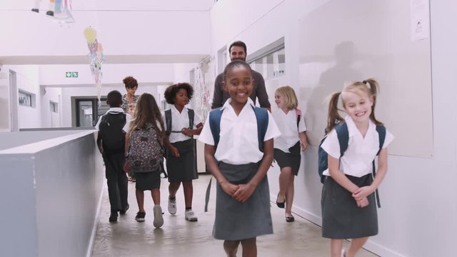 Teacher And Pupils Walking Along Corridor In Busy Elementary School Corridor