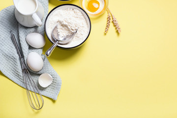Cooking and baking ingredients background on yellow paper, flour, eggs, whisk and milk
