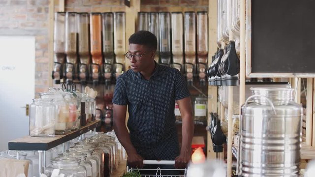 Young Man Looking At Products In Sustainable Plastic Free Grocery Store