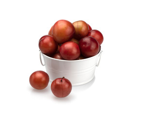 Ripe maroon plum in a white basin and near it on a white background. Isolated. Close-up. Still life.