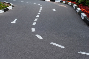 Asphalt road with a two-way marking and a curb.  White arrows indicate the direction of travel.
