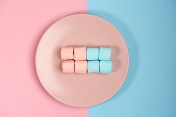 Pink plate with marshmallow, isolated on blue and pink, background. Top view.