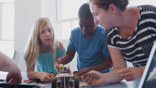 Two Students With Female Teacher In After School Computer Coding Class Learning To Program Robot Vehicle